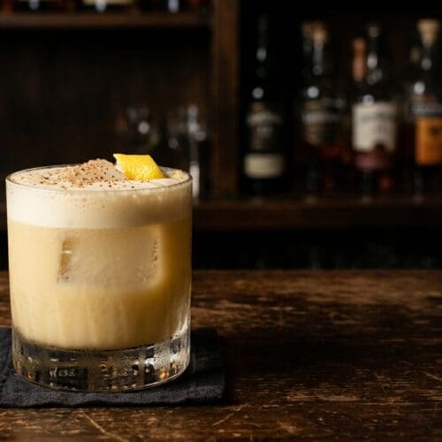 Soapy Tits cocktail in a rocks glass with a creamy foam cap on a dark bar